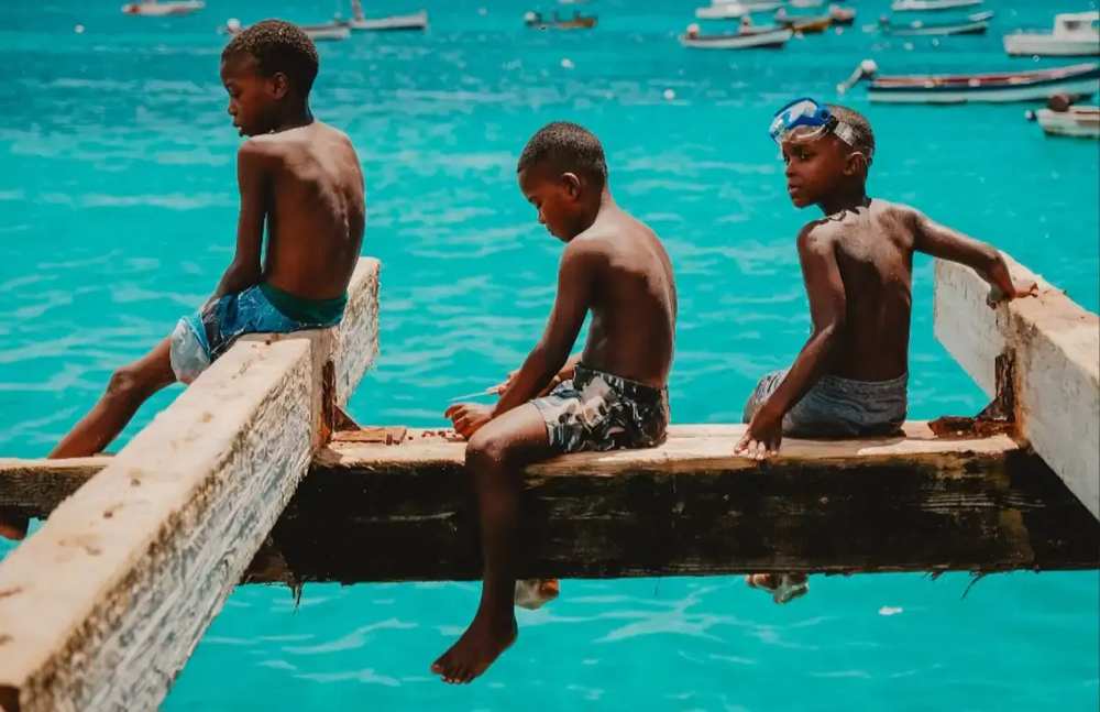 Crianças locais sentadas num cais de madeira junto ao mar