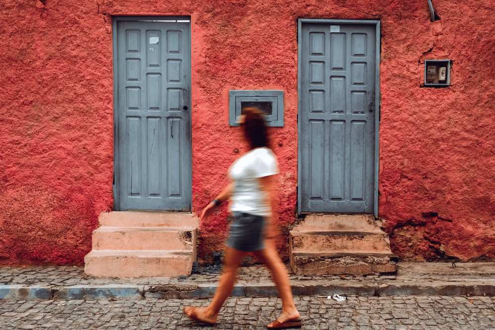 Mulher a caminhar junto a uma parede vermelha típica de Santa Maria